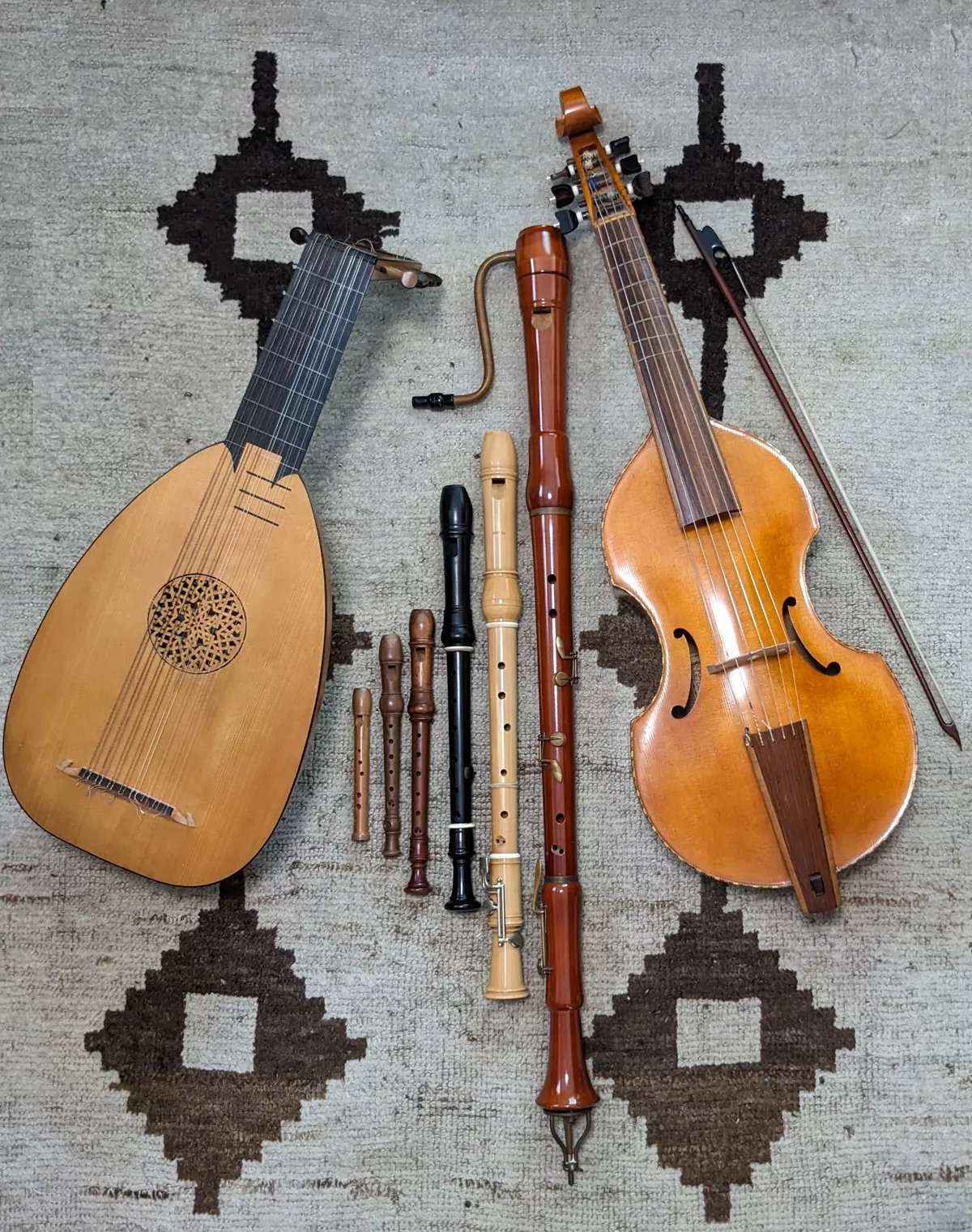 A viol, lute, and assortment of recorders of various sizes artfully laid out on a rug